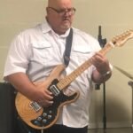 El pastor toca la guitarra al frente del santuario, guiando a la congregación en una adoración sincera y compartiendo la alegría de la música como un regalo para glorificar a Dios.