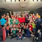 Miembros y visitantes de la iglesia se reúnen en mesas decoradas durante el banquete navideño, compartiendo comida, risas y el gozo del nacimiento de Cristo como una familia unida.