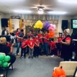 Niños con camisetas y gorras de la Escuela Bíblica de Verano se alinean con orgullo al frente de la iglesia, acompañados por sus líderes, celebrando un alegre momento de graduación lleno de fe.