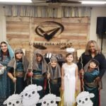 Niños vestidos como María, José, pastores, ovejas y ángeles posan con orgullo junto a los líderes adultos tras la obra navideña, celebrando el nacimiento de Jesús con creatividad y alegría.