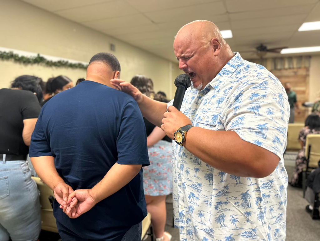 El pastor impone manos sobre un joven en oración, con el micrófono aún en la mano, simbolizando cómo el mensaje continúa en el ministerio personal. El momento refleja el cuidado y el poder de la oración en Vision Sinai.