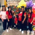 Maestros de la Escuela Bíblica de Verano sonríen frente a escenografías creativas, con camisetas y gorras a juego, representando el corazón y la dedicación del ministerio infantil en Vision Sinai.