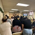 La congregación permanece de pie en silencio reverente, con la cabeza inclinada tras el sermón—abrazando el poder de la Palabra y la presencia del Espíritu Santo.