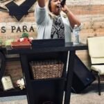 La líder de adoración Esthermary levanta una mano en alabanza mientras sostiene el micrófono con la otra, guiando con pasión a la congregación desde el púlpito de la iglesia.